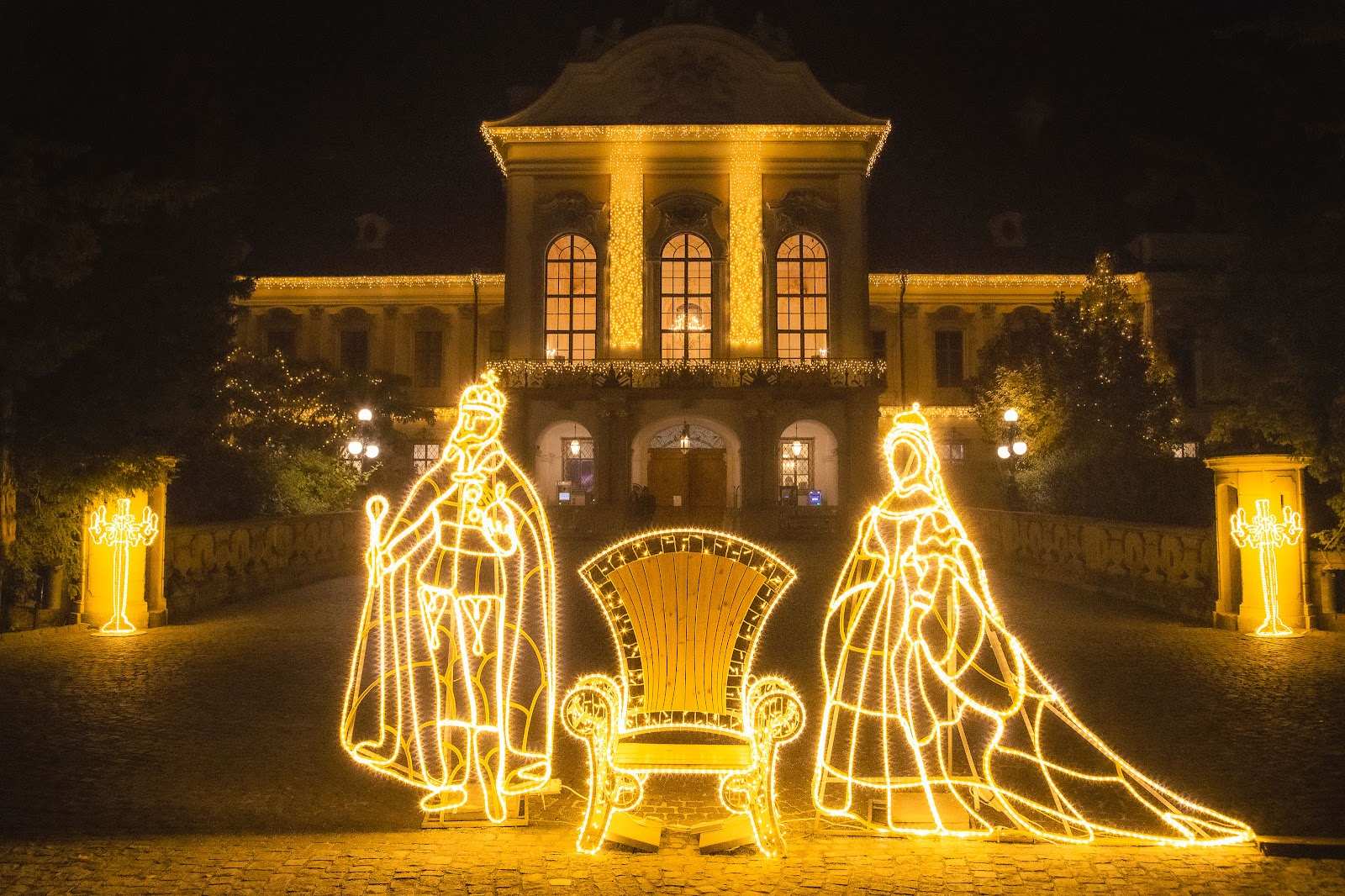 Leuchtende Figuren auf einem Rundweg vor einem beleuchteten Schloss